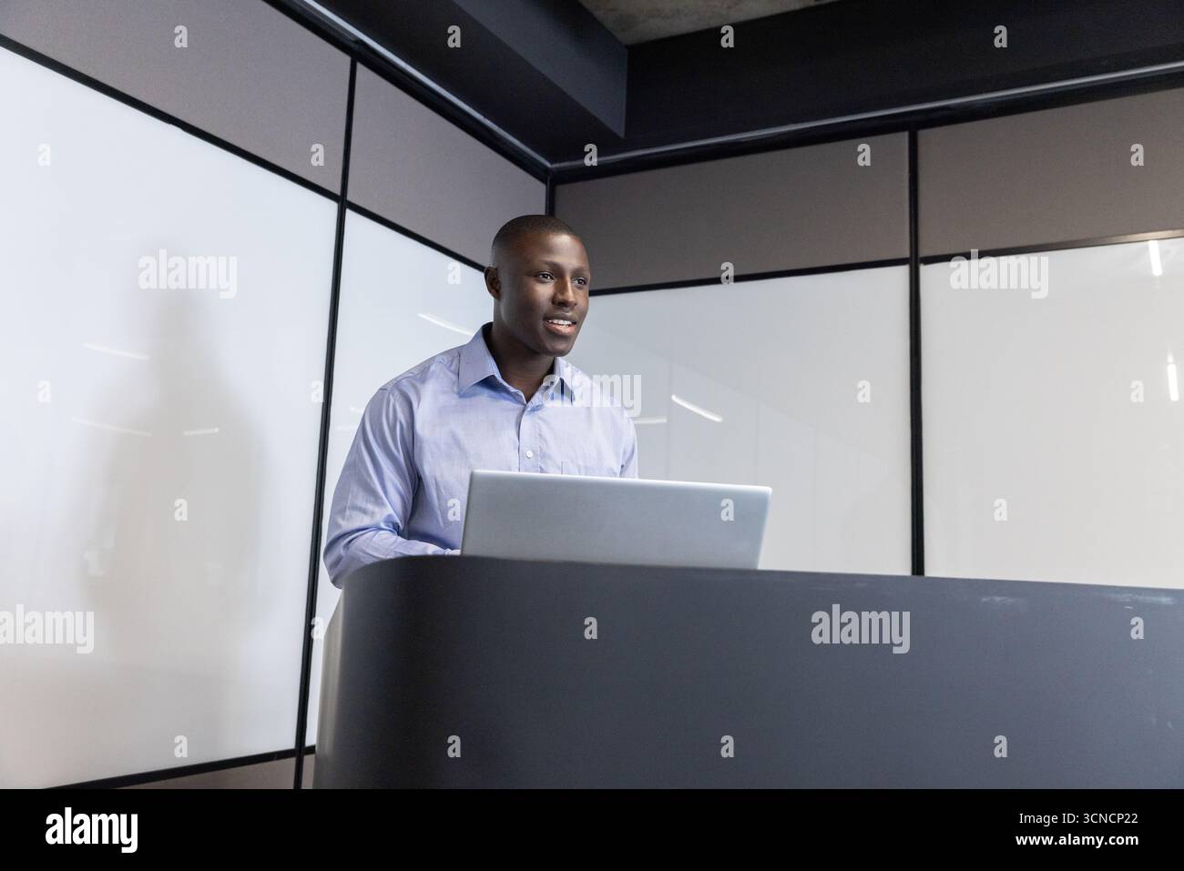 afroamerikaner, der auf dem Podium im Konferenzraum mit matten Paneelen spricht, mit Laptop Stockfoto