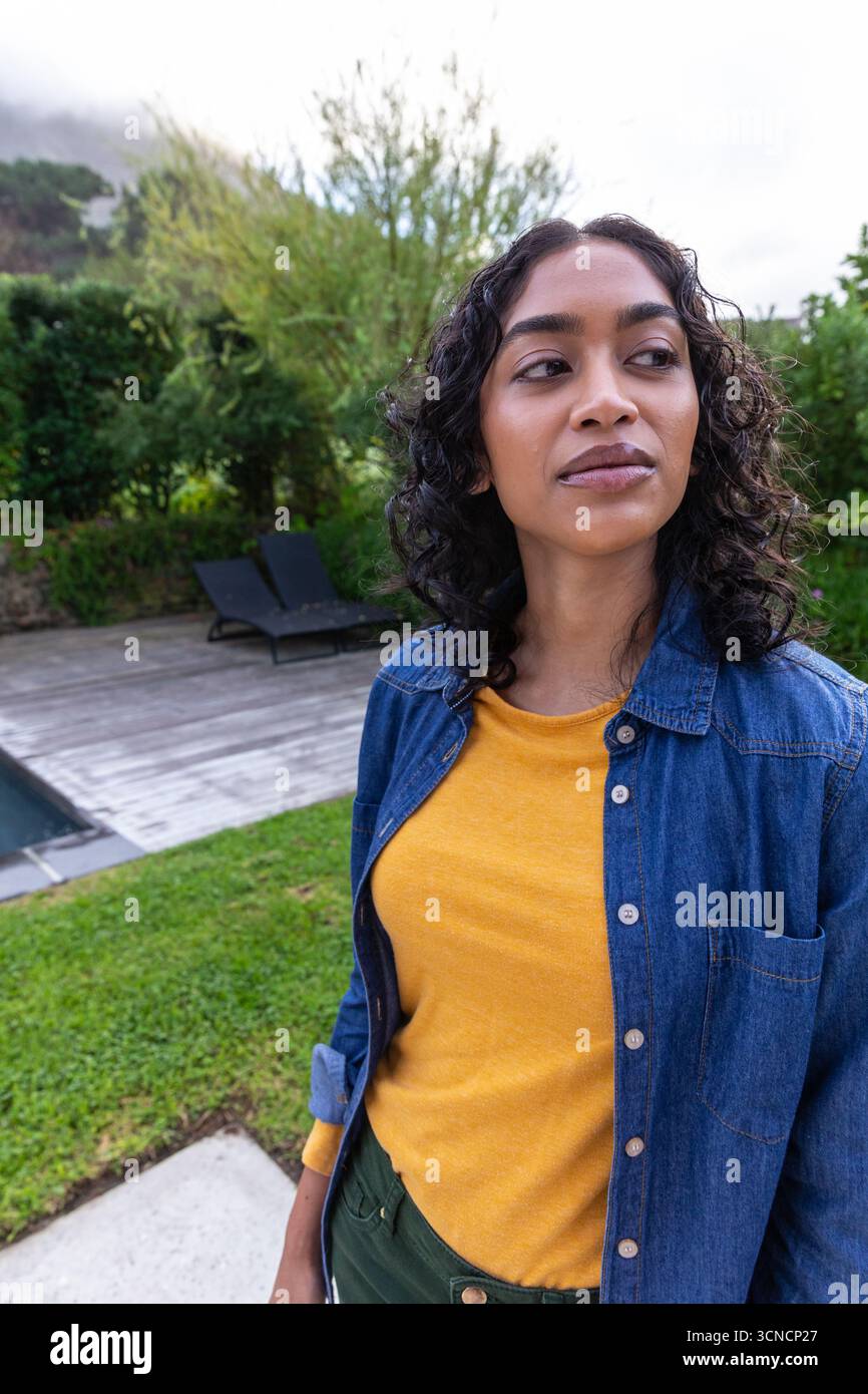 afroamerikanische Frau, die auf dem Garten in der Nähe des Pools steht, Terrasse mit schwarzen Stühlen, Kopierraum Stockfoto