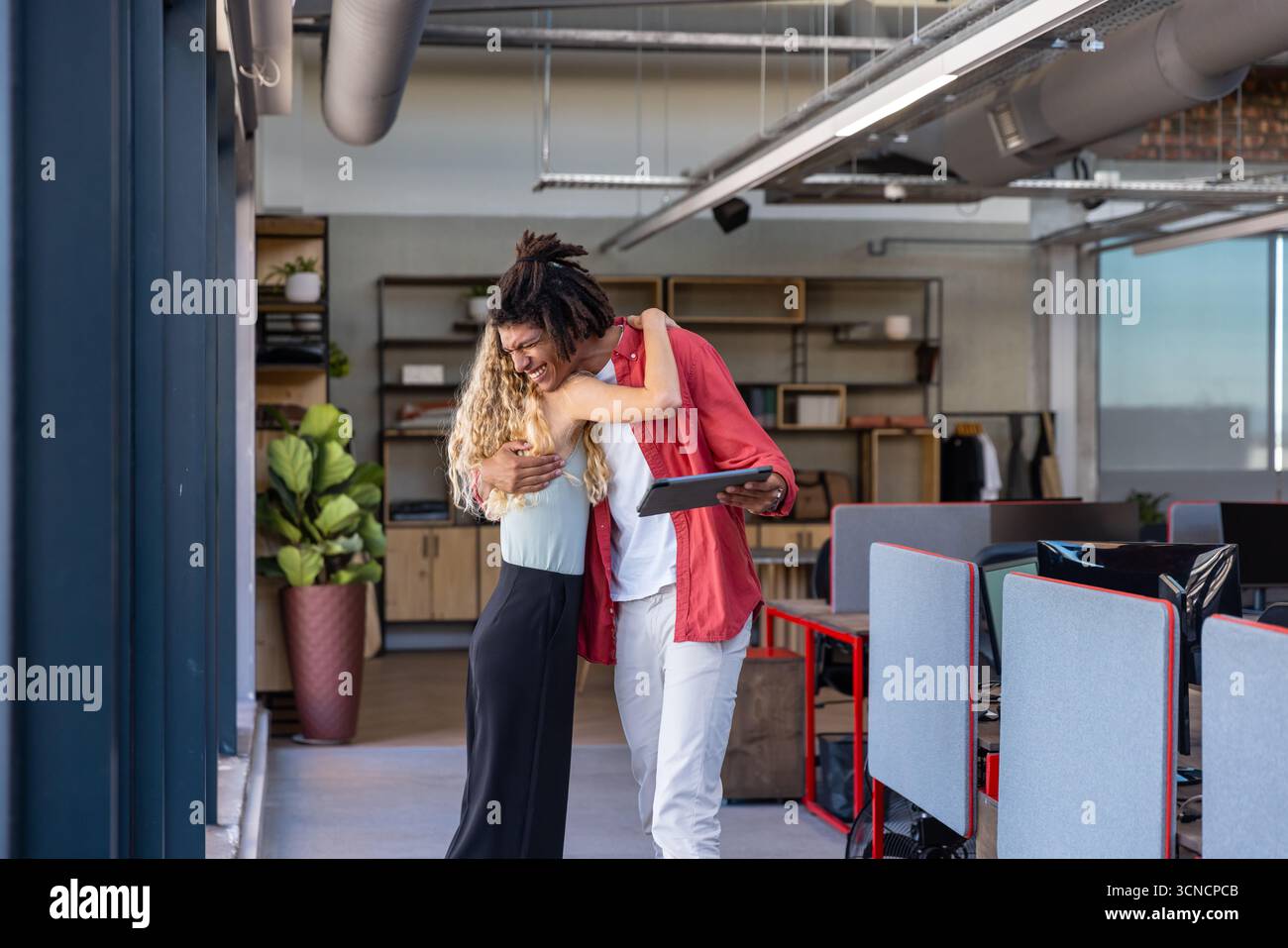 Verschiedene Kollegen, die sich in der Nähe von Workstations mit Stoffträger in Großraumbüros mit Tablet und Anlage umarmen Stockfoto
