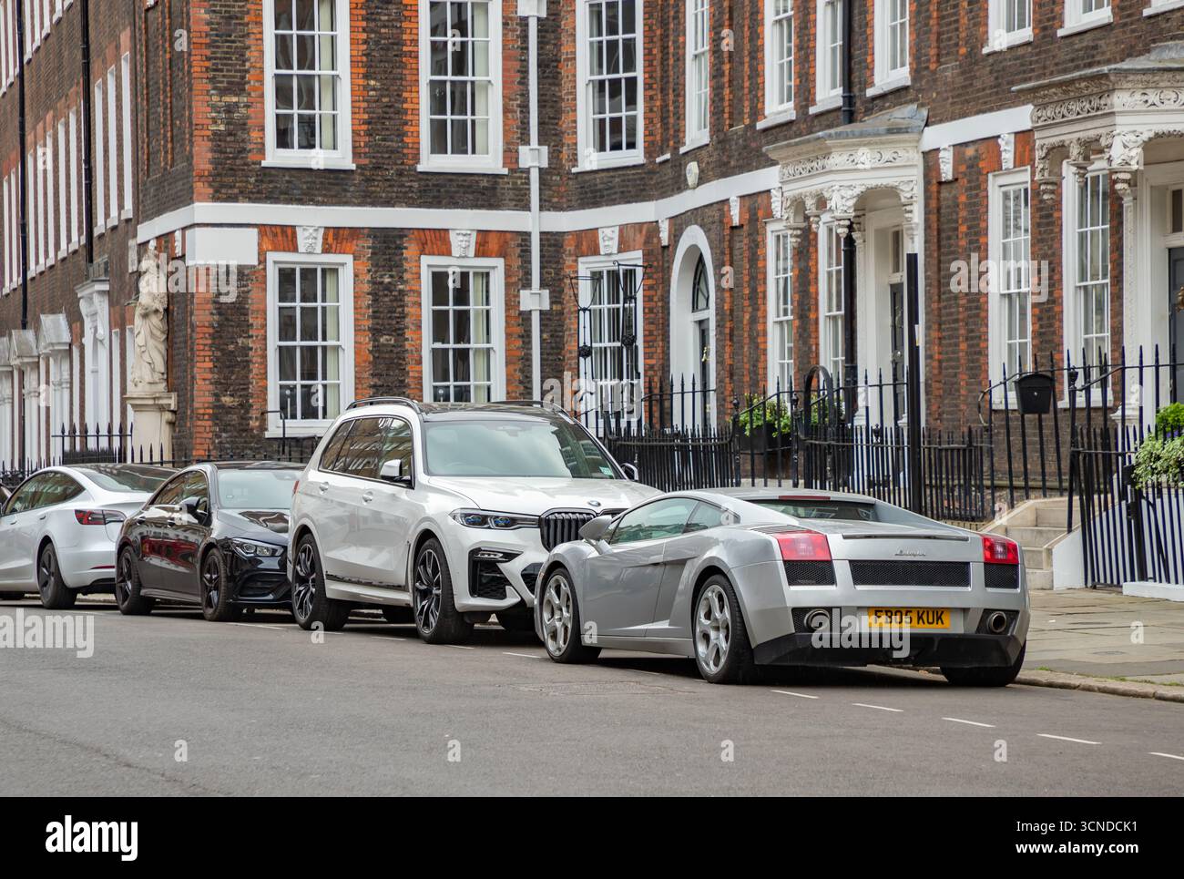 Ein Bild von einer Reihe lauter Autos, die vor viktorianischen Häusern in London geparkt sind. Stockfoto