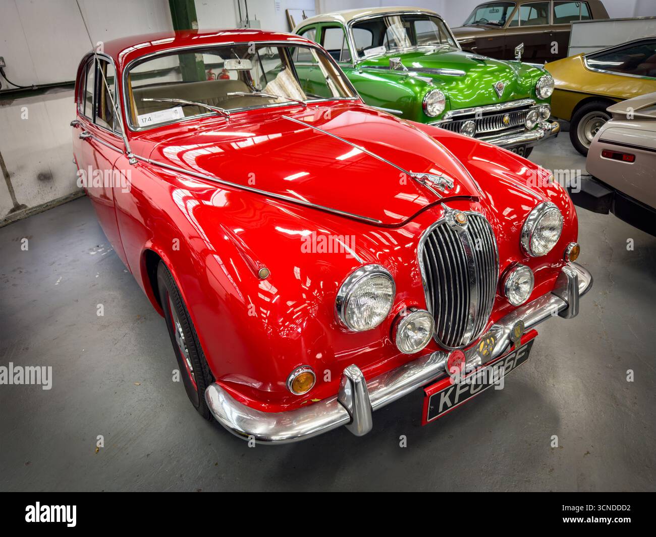 Klassisches rotes Jaguar Mark 2 Fahrzeug in einem Oldtimer-Ausstellungsraum mit verschiedenen historischen Autos im Hintergrund - Smartphone-aufgenommenes Stockfoto