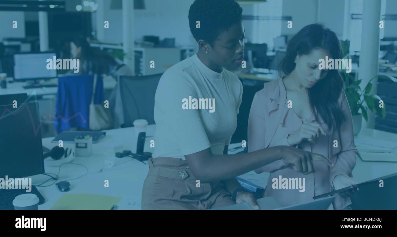 Sie zeigt auf den Laptop, Frau in weißem Oberteil, die mit einem Kollegen im Büro in rosa Blazer arbeitet Stockfoto