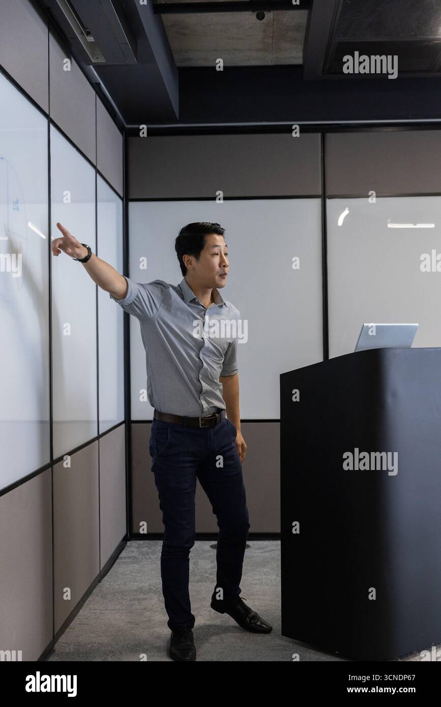 Präsentator steht neben Whiteboard und Podium, mit Laptop, Gesten im Besprechungsraum Stockfoto