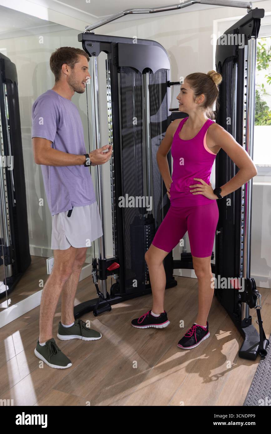 Ein Paar, das im Fitnessstudio am Fenster steht und über das Training mit dem Kabelgerät spricht, während es die Fitnessbänder überprüft Stockfoto