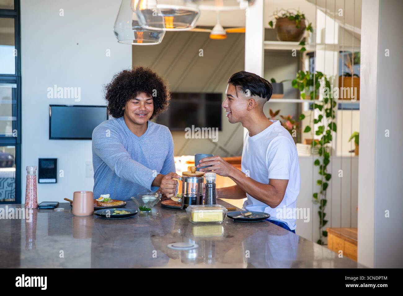 Verschiedene männliche Freunde, die auf der Kücheninsel French Press Kaffee gießen und sich bei Avocado Toast unterhalten Stockfoto