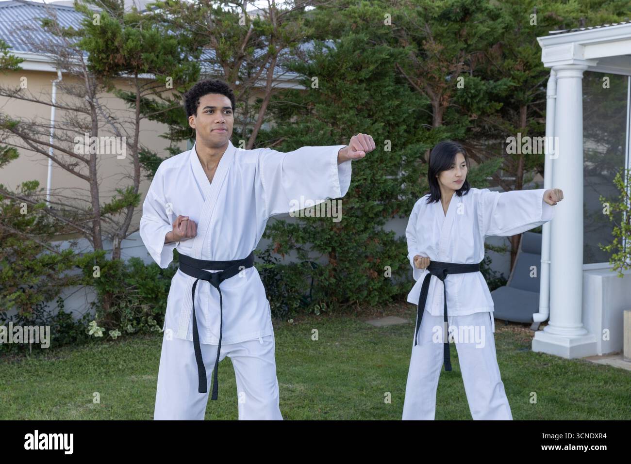 afroamerikaner und asiatische Frau üben Karate im Hinterhof in gis und Gürteln Stockfoto