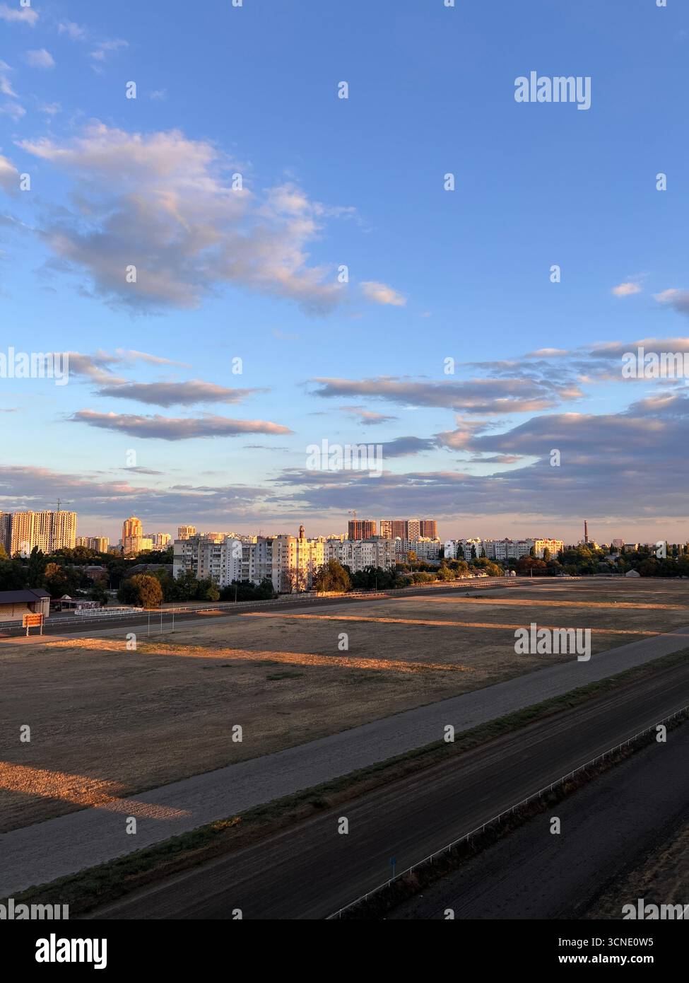 Sonnenuntergang über der Stadt, wunderschöne goldene Strahlen der untergehenden Sonne über der Rennstrecke - Smartphone-aufgenommenes Stockfoto
