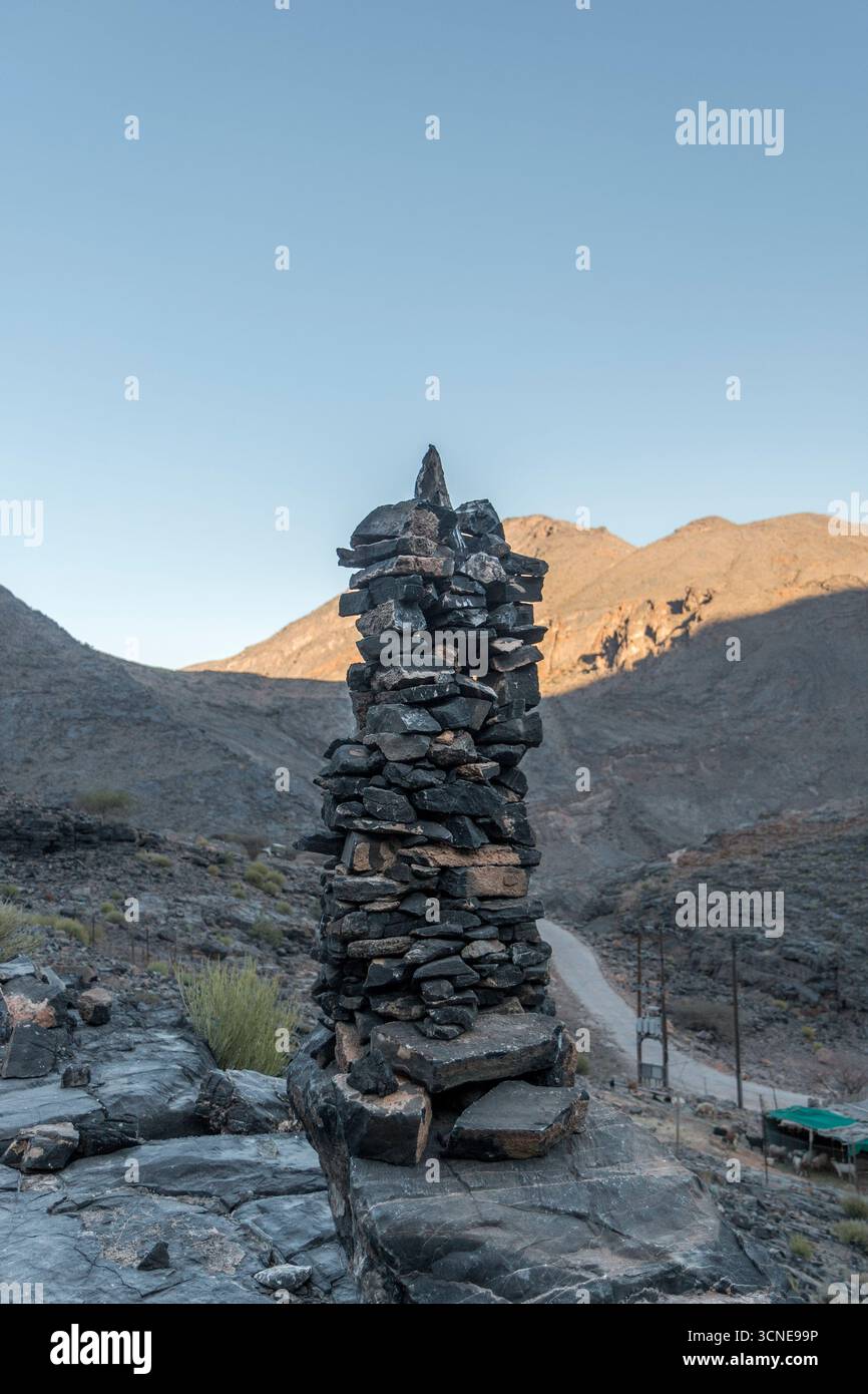 Oman - Al Hamra - Bilad Sayt - Ein trockener Steinhaufen steht in der Abenddämmerung als Wächter, während goldenes Licht die gefalteten Grate um den Pass bürstet. Stockfoto