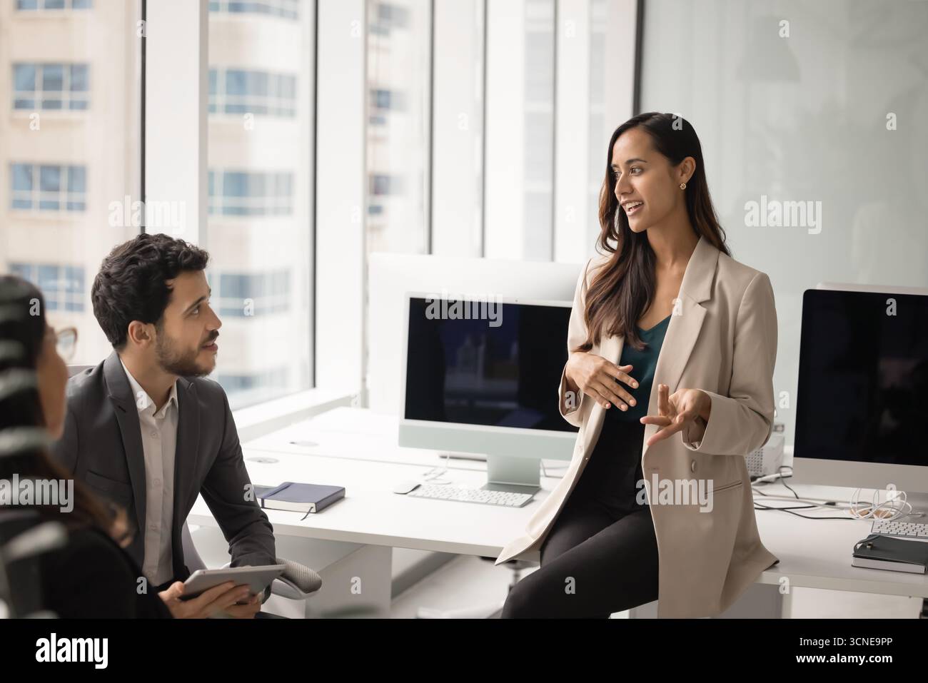 Positive junge Projektmanagerin, die beim Meeting mit Kollegen spricht Stockfoto