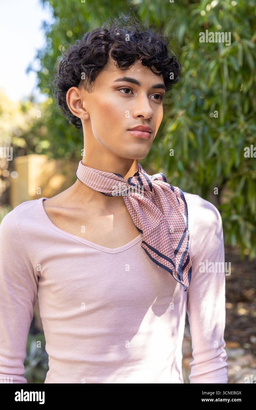 Asiatischer Mann, der im Garten mit Laub steht und einen rosafarbenen Schal und Ohrringe trägt Stockfoto