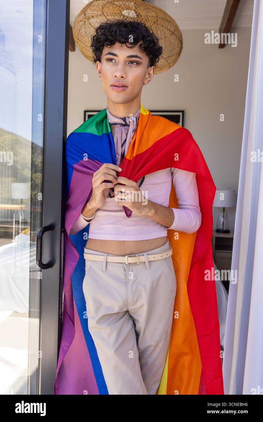Asiatischer Mann, der in einer Glasschiebetür steht, oben, Regenbogenfahne und Schal trägt Stockfoto