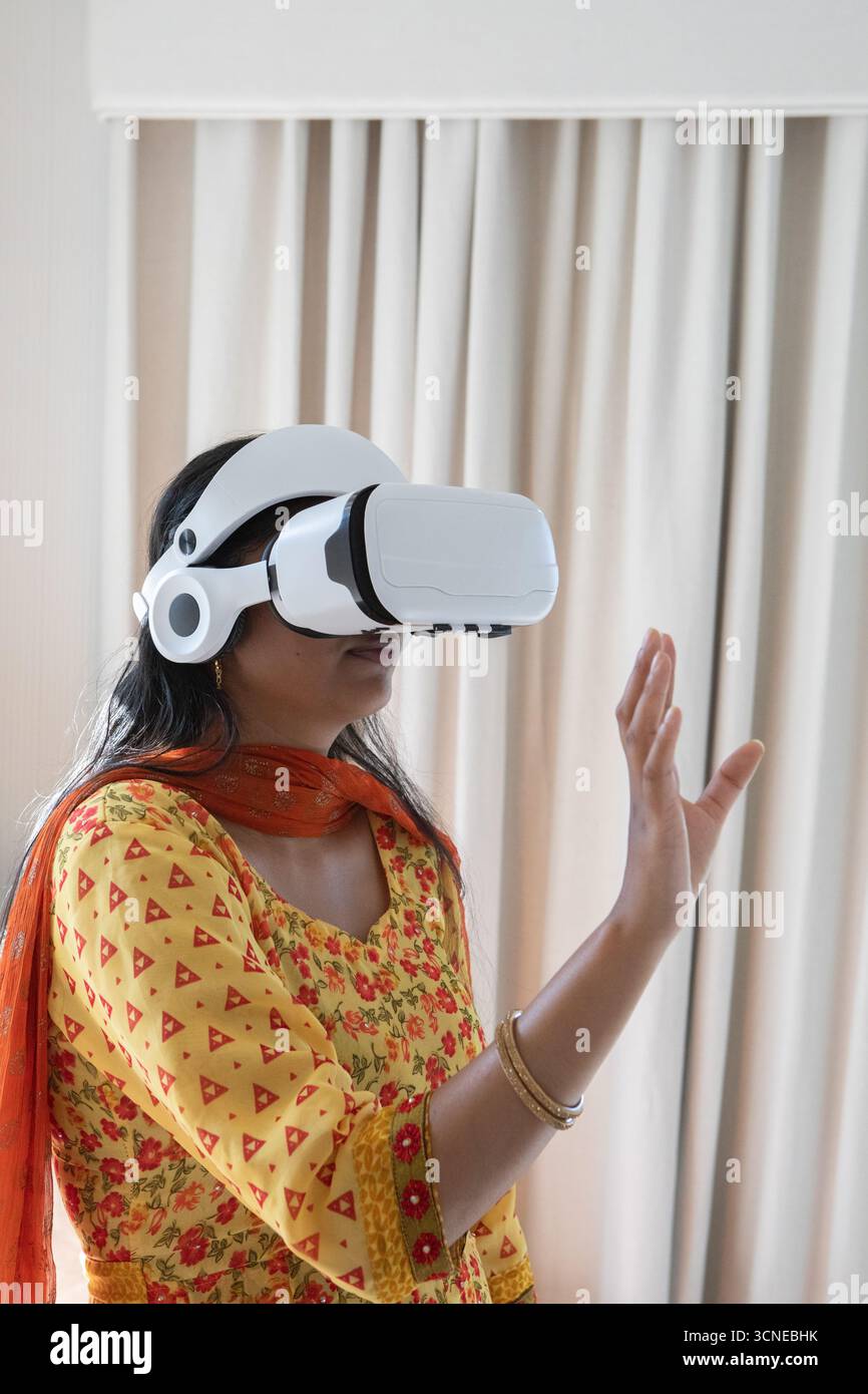 Indische Frau trägt gelbe Kurta, vr-Headset erreicht Schnittstelle im Raum, Kopierraum Stockfoto