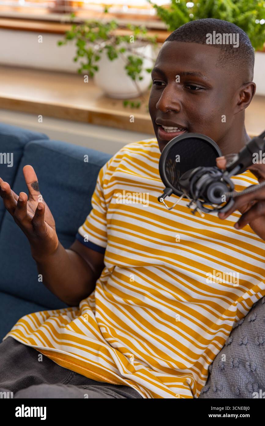 afroamerikaner, der auf blauer Couch in Popfilter-Mikrofon spricht, Gesten Stockfoto