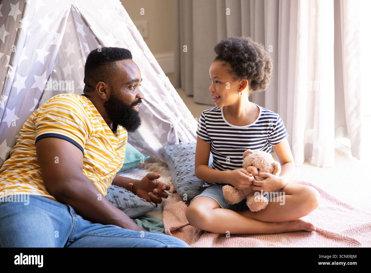 Afroamerikaner Vater und Tochter sprechen in der Heimspielecke mit Sternzelt und Teddybär Stockfoto