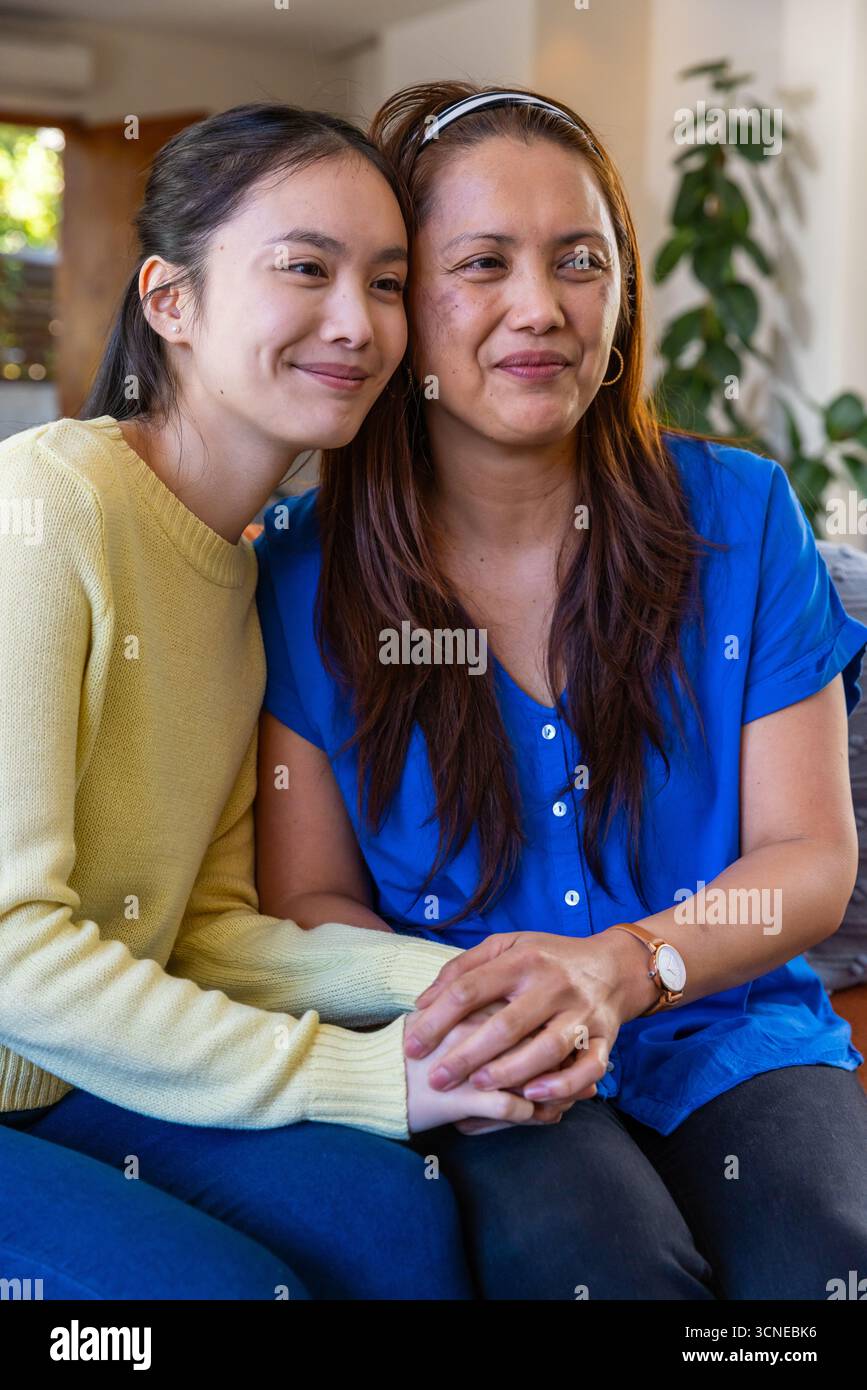 Asiatische Mutter und Tochter sitzen auf dem Sofa und halten die Hände unter einem Holzfenster Stockfoto
