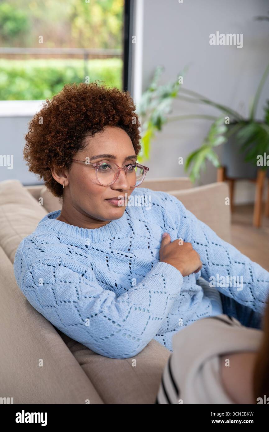 afroamerikanerin, die sich im Wohnzimmer auf dem Sofa liegend und eine Brille und einen blauen Pullover trug Stockfoto