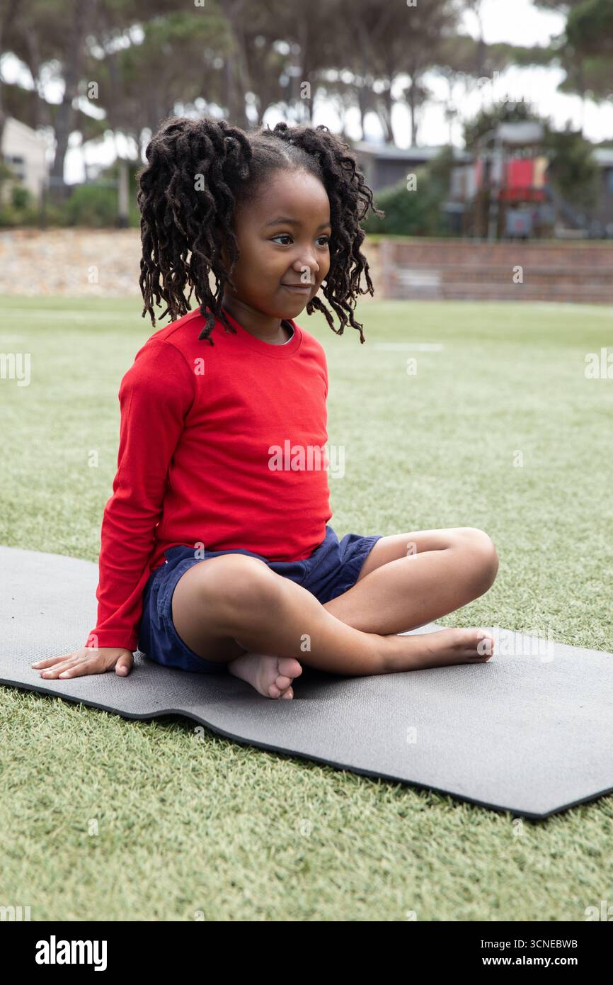 afroamerikanisches Mädchen in roter Marine-Shorts sitzt im Kreuz auf dunkler Matte auf dem Spielplatz Stockfoto