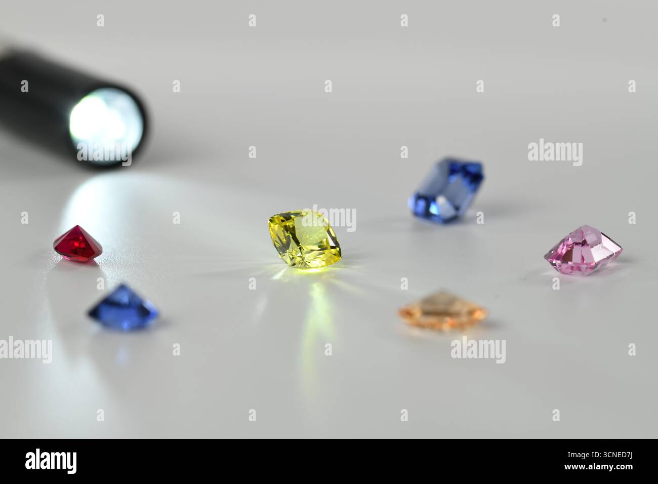Eine Sammlung von Edelsteinen wird durch eine Taschenlampe beleuchtet. Die Edelsteine haben verschiedene Farben, darunter blau, gelb und pink Stockfoto