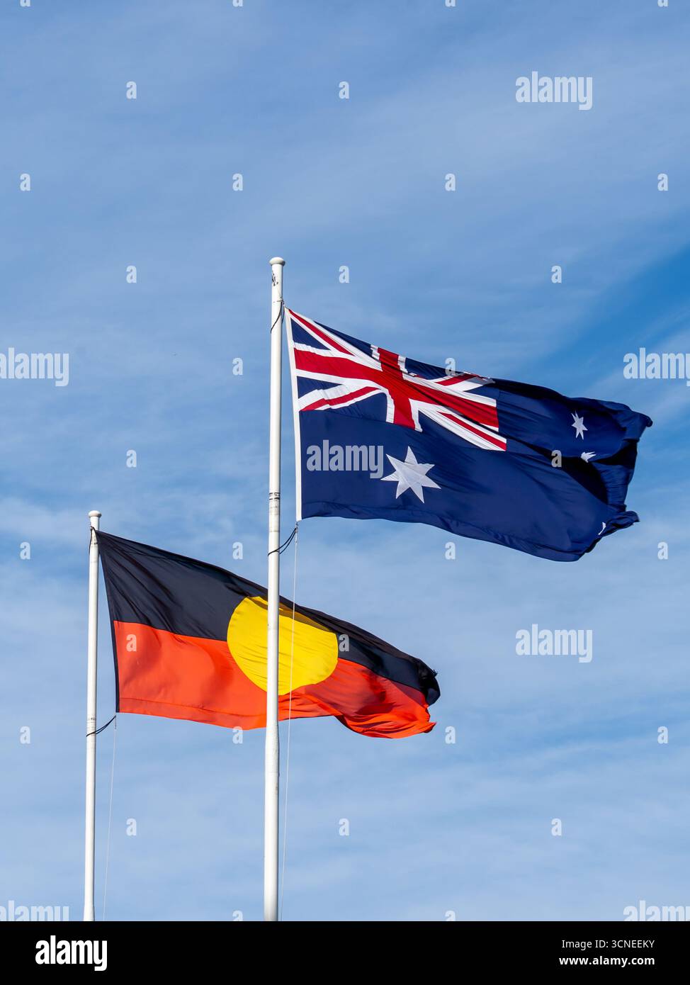 Australische Nationalflagge und Flagge der australischen Aborigines, die mit blauem Himmel im Hintergrund winken Stockfoto