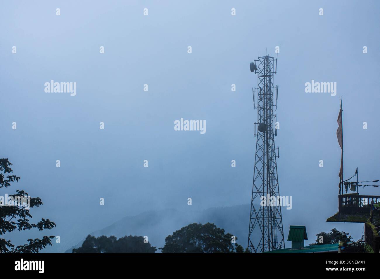 Telekommunikationsturm, der in einem nebeligen Berggebiet auftaucht, symbolisiert Konnektivität in ländlichen Gebieten. Stockfoto