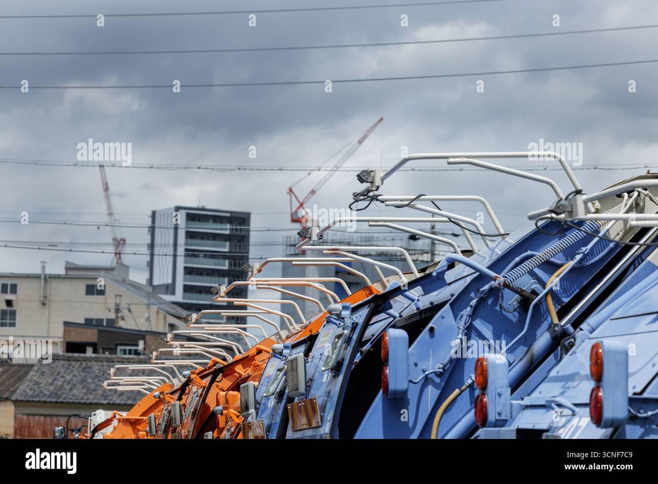Makellos saubere Müllwagen ruhen während der Ausfallzeit am Wochenende aus. Weiße Querlenker sitzen offen über den farbenfrohen Karosserien des Trucks, die urbane Elemente zeigen. Stockfoto