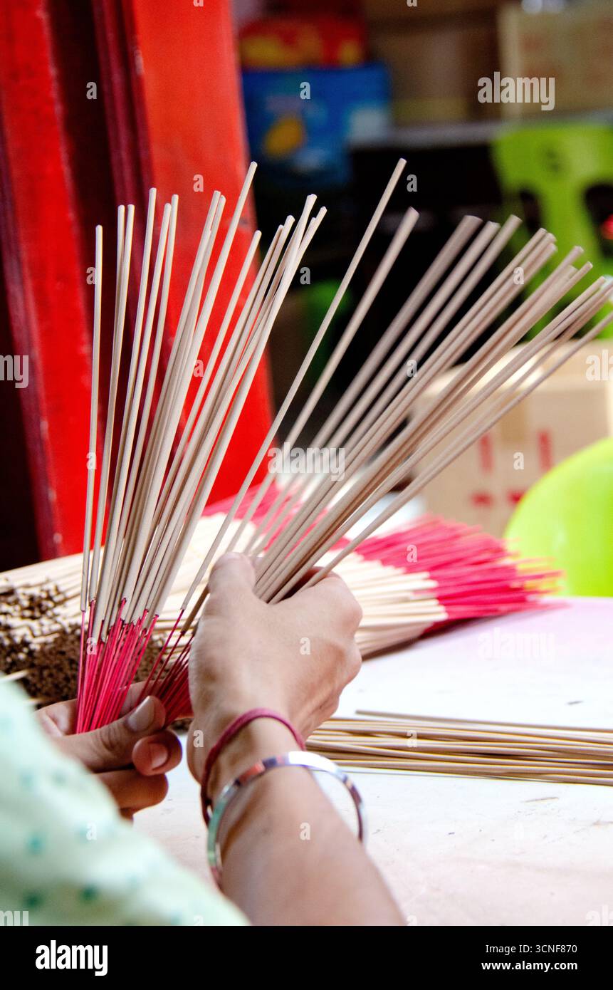Nahaufnahme von Händen, die Räucherstäbchen mit roten Basen halten und arrangieren, die häufig in religiösen Ritualen und kulturellen Zeremonien in ganz Asien verwendet werden. Stockfoto