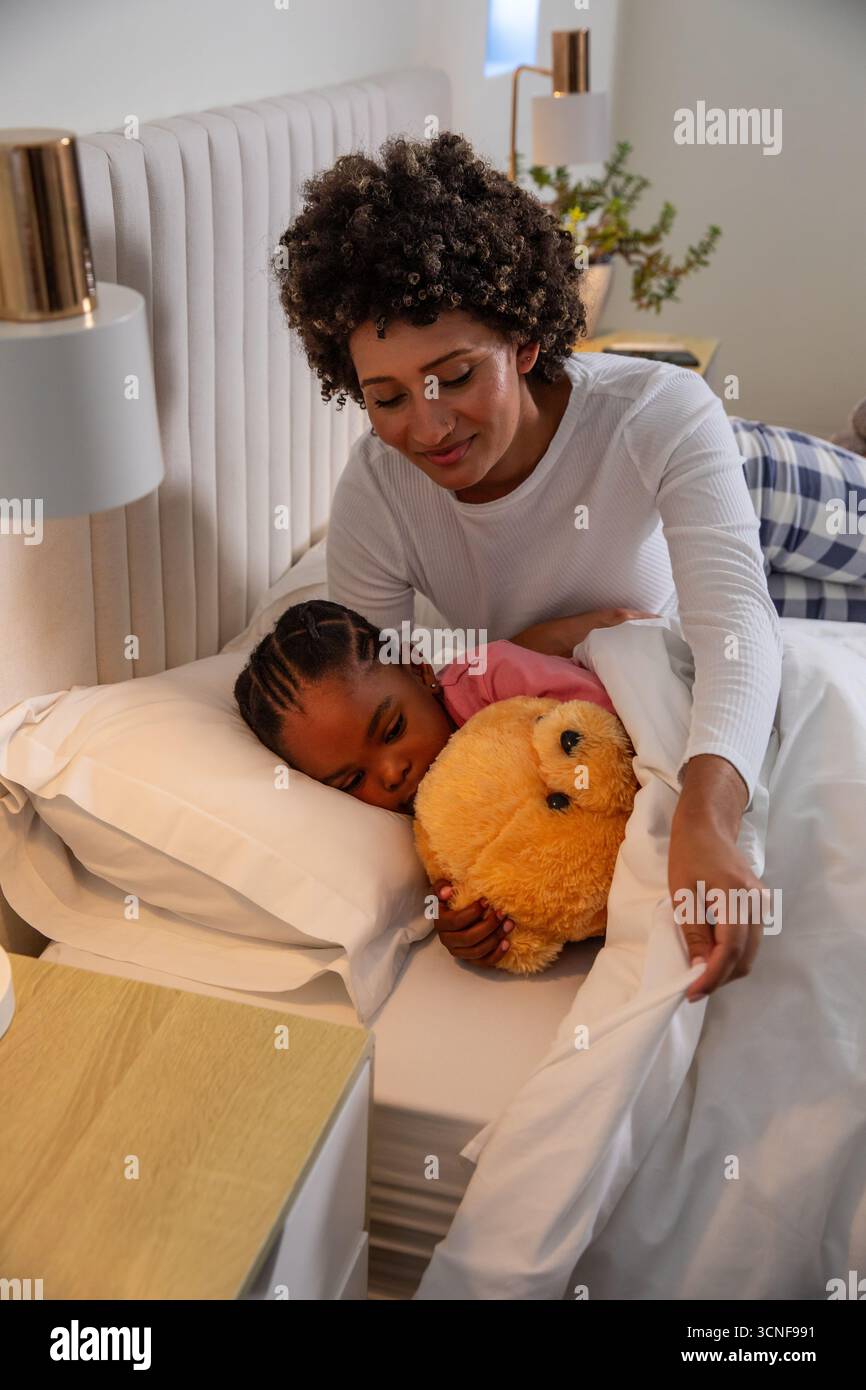 Im Schlafzimmer mit getuftetem Kopfteil und Tischlampe stehen Mutter und Kind im Bett Stockfoto