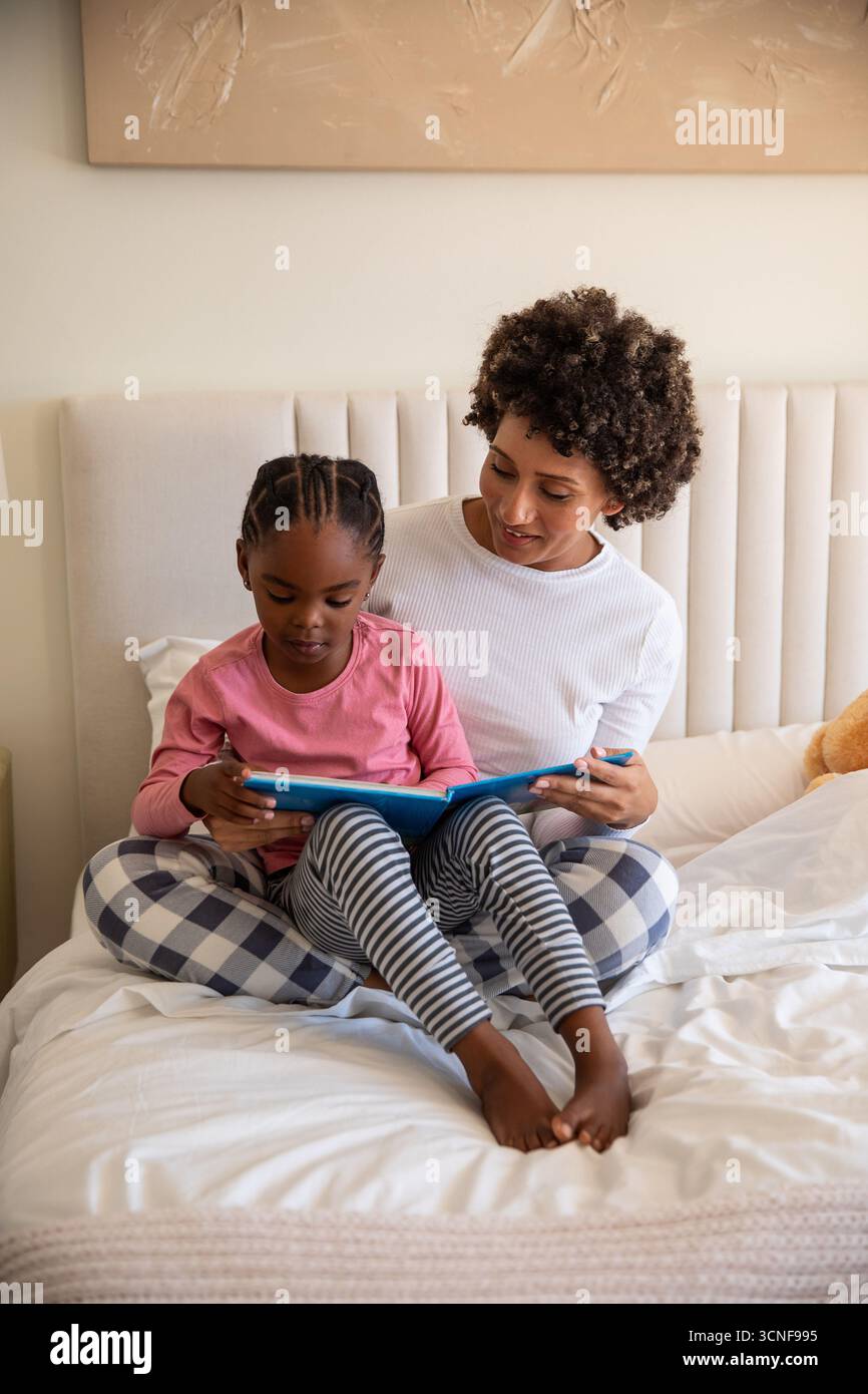 afroamerikanische Mutter mit Tochter liest blaues Buch auf Bettdecken mit Teddybären Stockfoto
