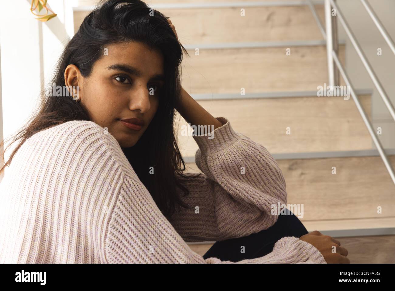 Indianerin sitzt auf einer modernen Holztreppe mit Metallgeländer, lehnt sich und blickt nach vorne Stockfoto