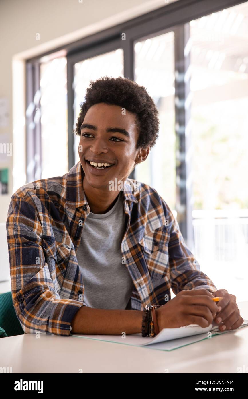 Afroamerikaner sitzt am weißen Tisch im Arbeitszimmer mit gelbem Stift auf Notizbuch und trägt Armbänder Stockfoto