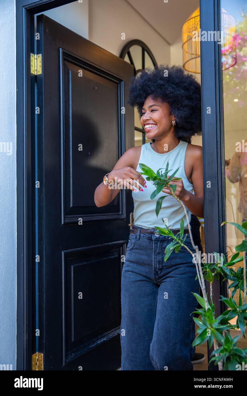 Topfpflanzen auf der Schwelle einer offenen schwarzen Tür mit goldenen Scharnieren an der Fassade Stockfoto