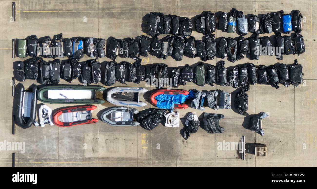 Ein Blick auf kleine Boote und Außenbordmotoren, die von Menschen benutzt werden, die als Migranten gedacht sind, um den Ärmelkanal von Frankreich aus in einem Lagerhaus in Dover, Kent, zu überqueren. Bilddatum: Sonntag, 21. September 2025. Stockfoto