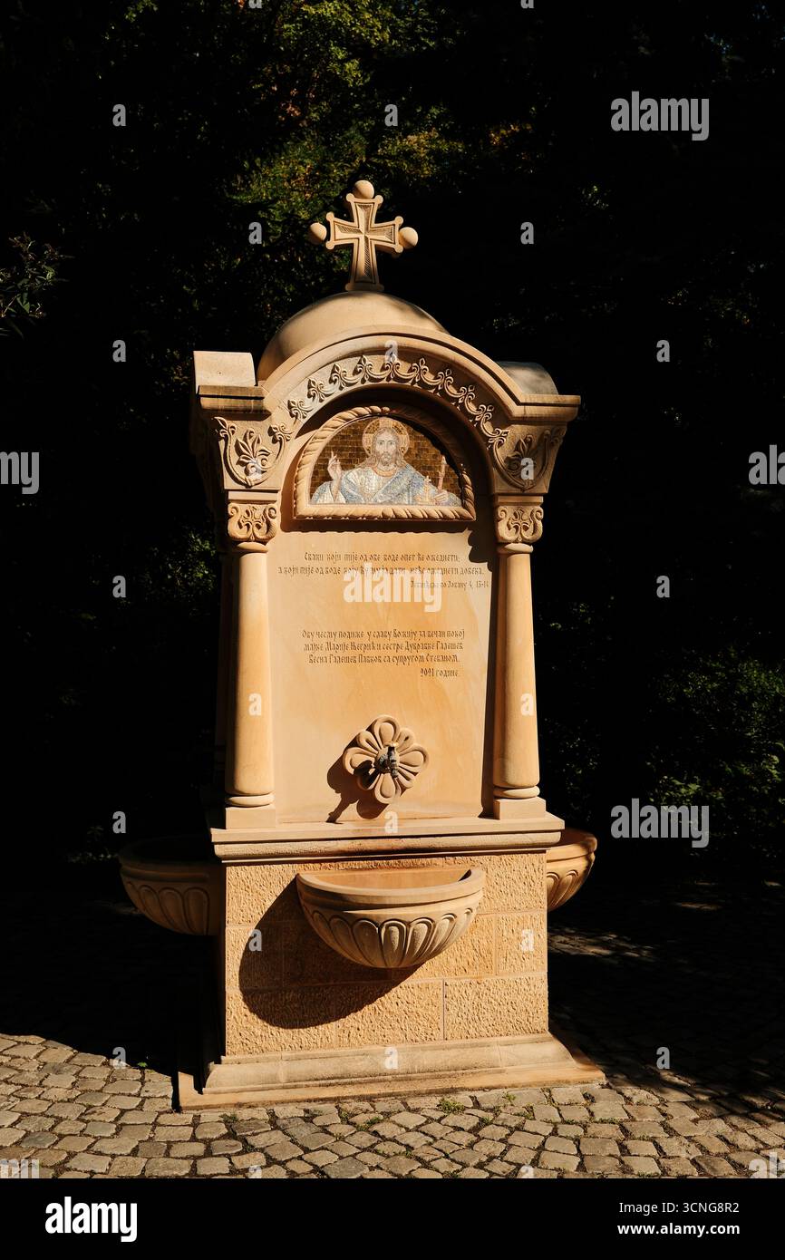 Steinbrunnen mit Kreuz und Mosaik von Jesus im Kloster Grgeteg in Fruska Gora. Novi Sad, Serbien - 19. September 2025. Stockfoto