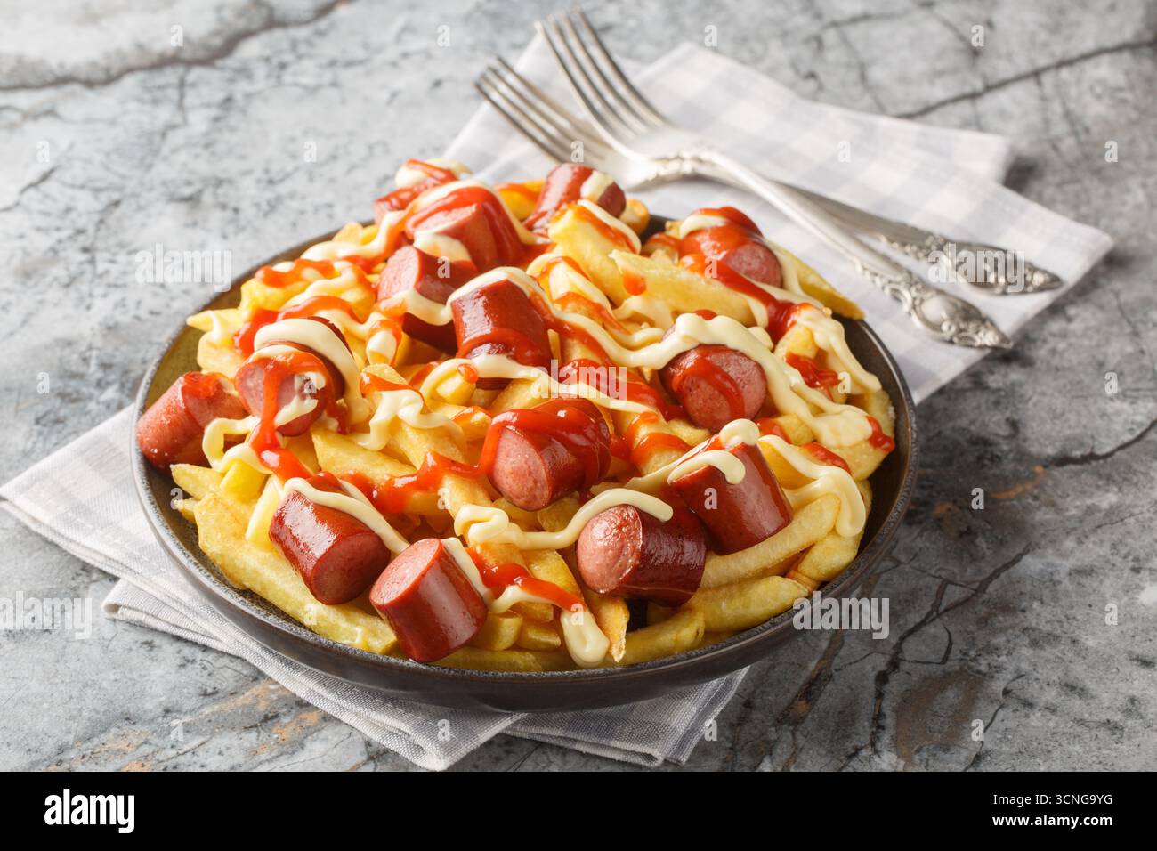 Salchipapa ist ein beliebtes peruanisches Rezept mit Pommes frites, serviert mit Rindfleischwürsten, garniert mit Soße aus der Nähe auf dem Teller auf dem Tisch. Horizontal Stockfoto