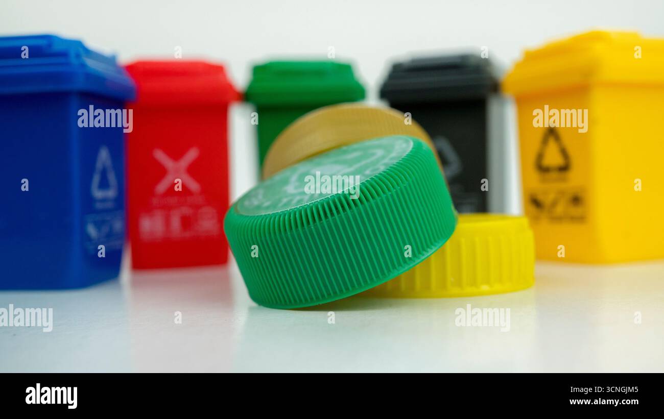 Plastikflaschen-Verschlüsse im Fokus mit Mülltonnen im Hintergrund, die die globale Krise der Umweltverschmutzung durch Mikrokunststoffe und die Herausforderungen beim Recycling darstellen. Konz Stockfoto