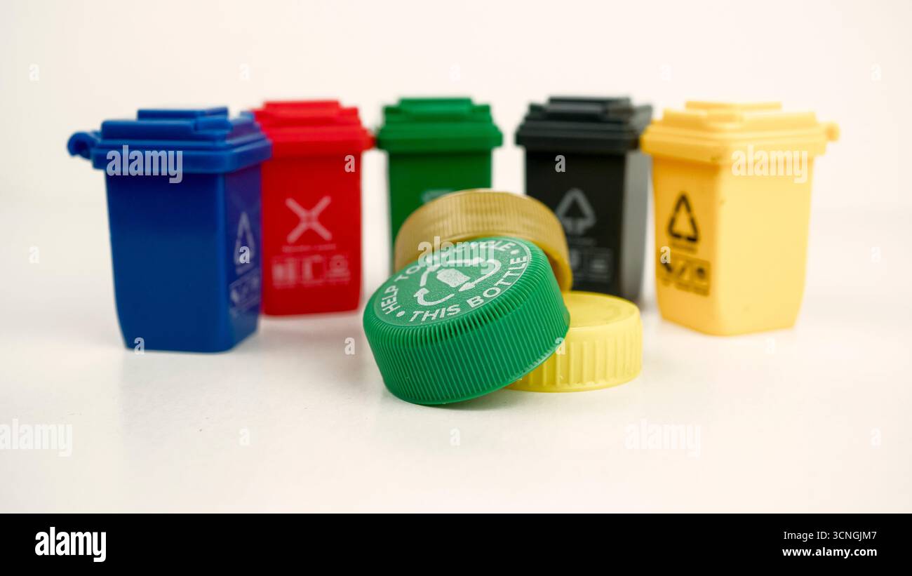 Plastikflaschen-Verschlüsse im Fokus mit Mülltonnen im Hintergrund, die die globale Krise der Umweltverschmutzung durch Mikrokunststoffe und die Herausforderungen beim Recycling darstellen. Konz Stockfoto