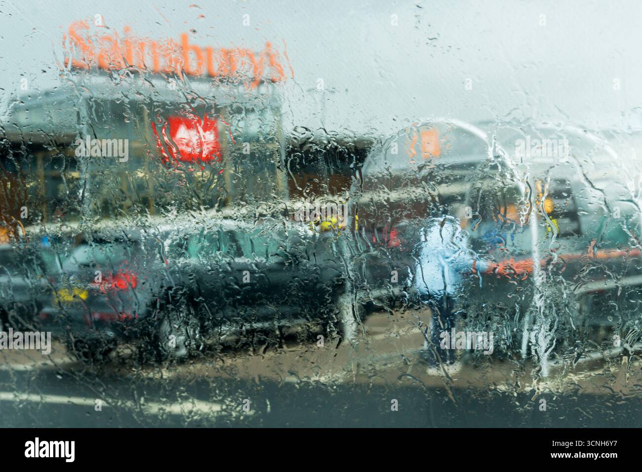 Supermarkt Shopping im Regen. Der Shopper gibt den Wagen während eines Regensturms auf dem Parkplatz von Sainsbury's zurück – durch ein nasses Fenster gesehen. Stockfoto