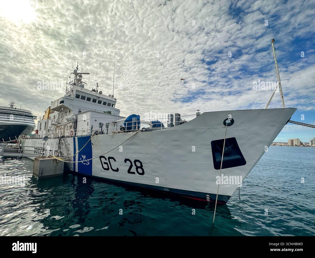 Ein Schiff der argentinischen Küstenwache legte neben einem Kreuzfahrtschiff am Puerto Madryn Pier an, mit türkisfarbenem Wasser und patagonischer Küste im Hintergrund Stockfoto