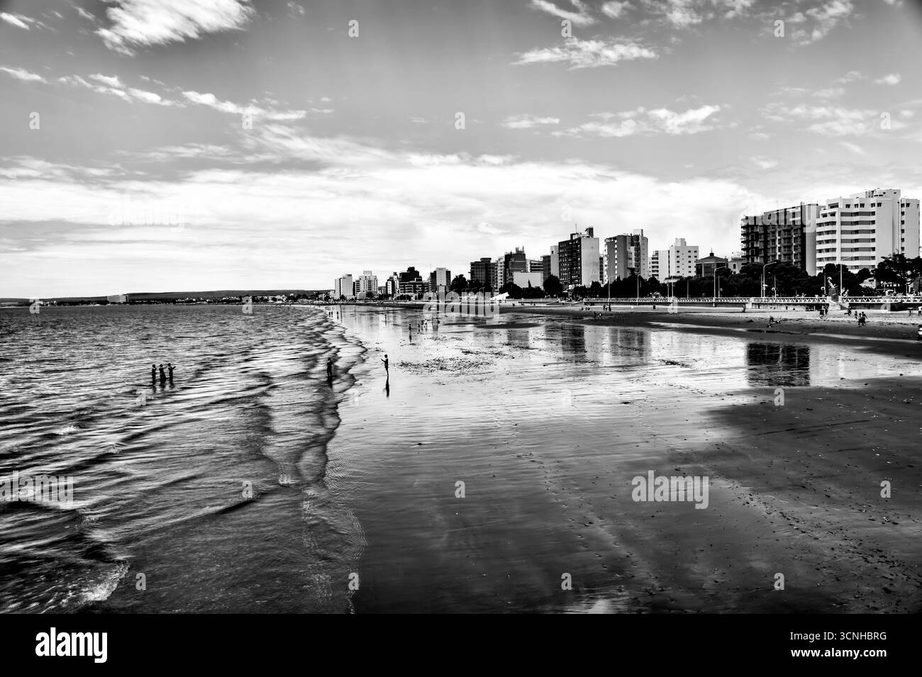 Zwei Figuren spazieren entlang des riesigen, windgepeitschten Strandes von Puerto Madryn, während sich stimmungsvolle Wolken über die patagonische Küste erstrecken. Stockfoto