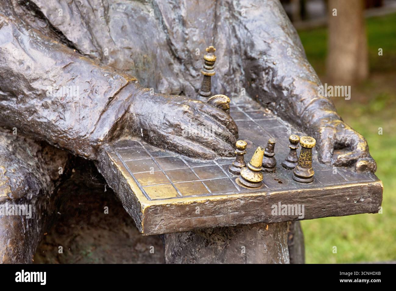 Nahaufnahme einer bronzenen Schachspielerstatue, die einen strategischen Schritt auf einem Schachbrett macht und das intellektuelle Spiel zeigt Stockfoto