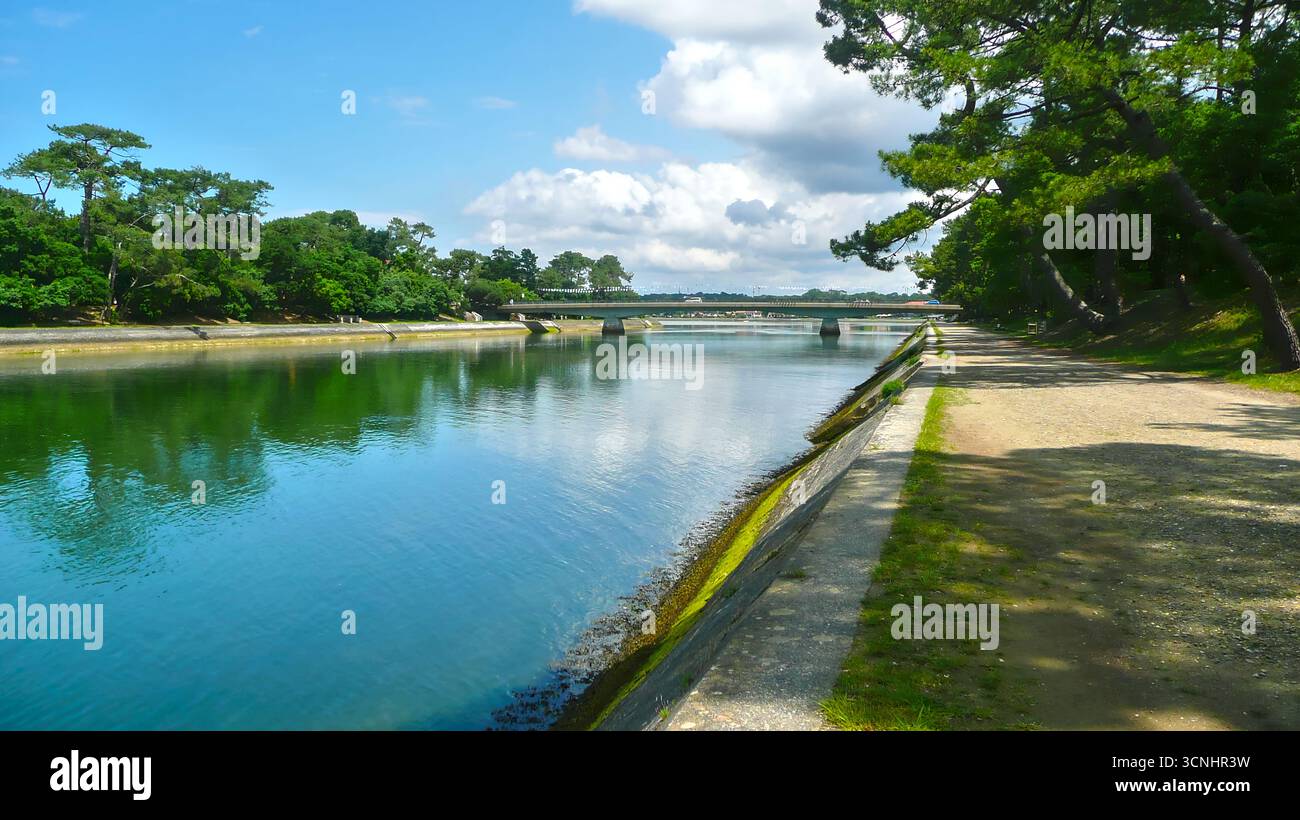 Blick auf den Canal d’Hossegor in Frankreich, mit ruhigem Wasser unter einem blauen Himmel mit verstreuten Wolken, umgeben von grüner Vegetation, von einer Wide erfasst Stockfoto