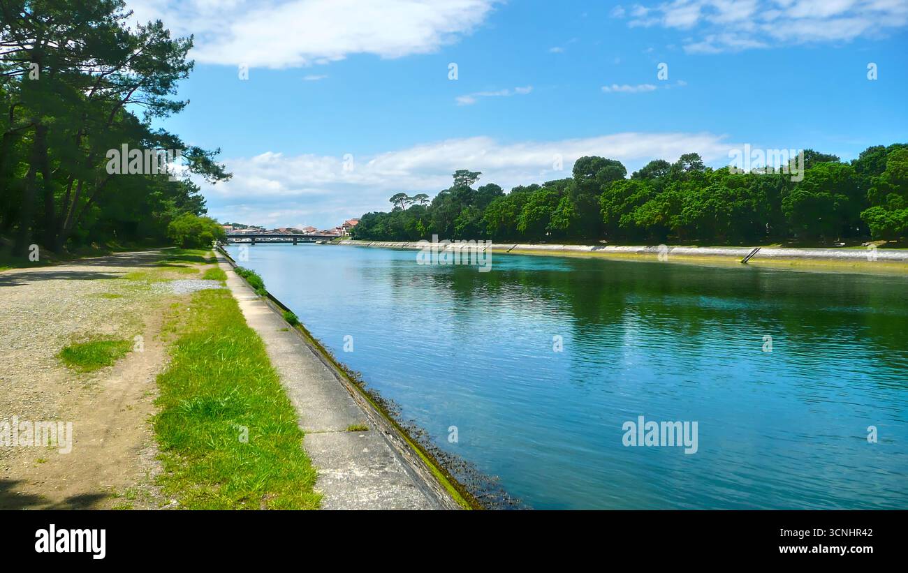 Blick auf den Canal d’Hossegor in Frankreich, mit ruhigem Wasser unter einem blauen Himmel mit verstreuten Wolken, umgeben von grüner Vegetation, von einer Wide erfasst Stockfoto