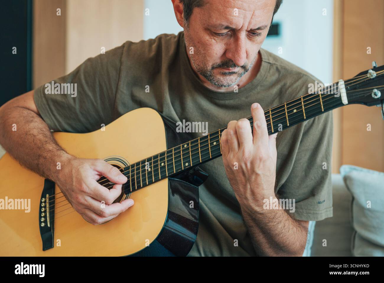 Amateurmusiker, der zu Hause Akustikgitarrenspiele, lässiges Lifestyle und kreatives Konzept übt und lernt. Selektiver Fokus. Stockfoto