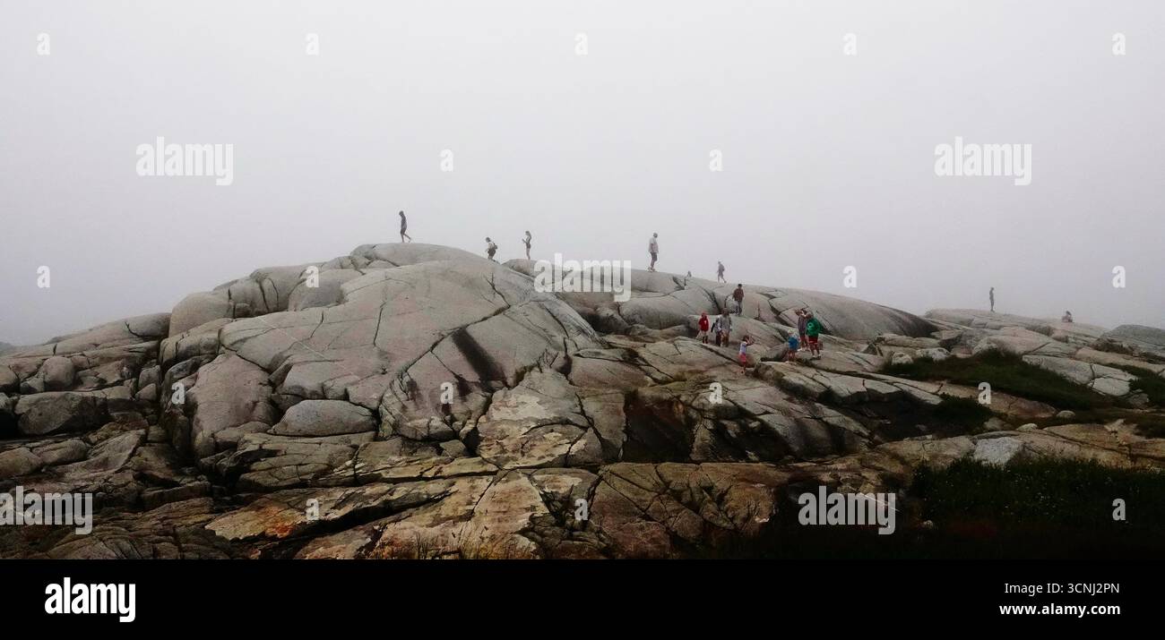 Menschen werden auf großen, glatten Felsen in Peggy's Cove Nova Scotia gesehen, während sie von dickem Nebel umgeben sind. Die Szene fängt ein Gefühl von Abenteuer und ein Stockfoto