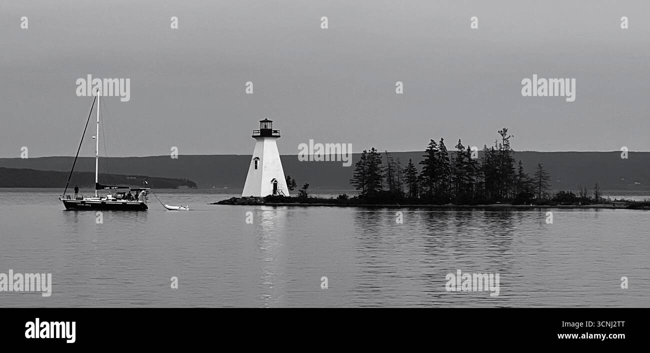 Ein wunderschönes Segelboot gleitet durch die ruhigen Gewässer von Bras d'Or neben dem Kidston Island Lighthouse in der Stadt Baddeck in Nova Scotia unter blauem Himmel. T Stockfoto