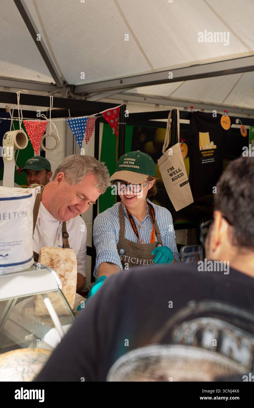 Lächelnde Käseverkäufer mit grünen Kappen interagieren mit Kunden unter dem Marktzelt beim Cheese 2025 Festival in Bra. Die zweijährliche Slow Food-Veranstaltung Showc Stockfoto