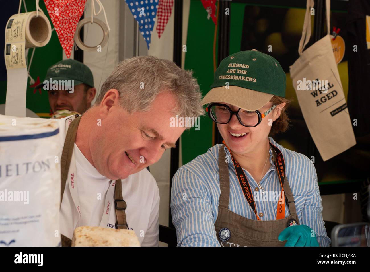 Professionelle Käseverkäufer tragen auf ihrem Marktstand während des Cheese 2025 Slow Food Festivals in Bra „Blessed Are the Cheesemakers“-Kappen. Display sh Stockfoto
