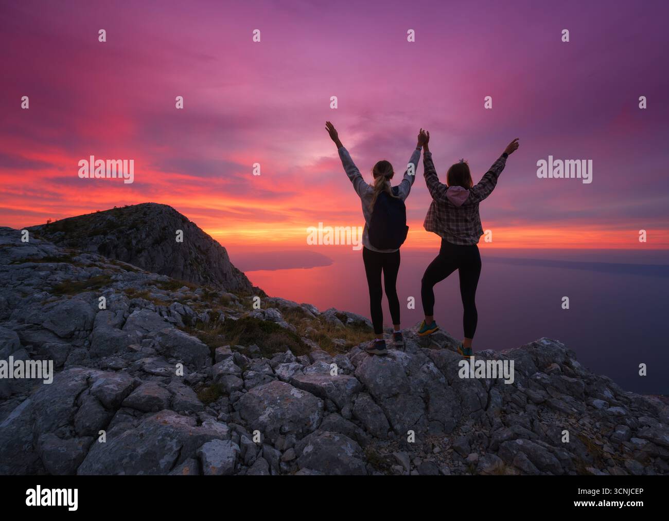 Frauen mit Rucksäcken und Arme auf dem Berg bei Sonnenuntergang Stockfoto
