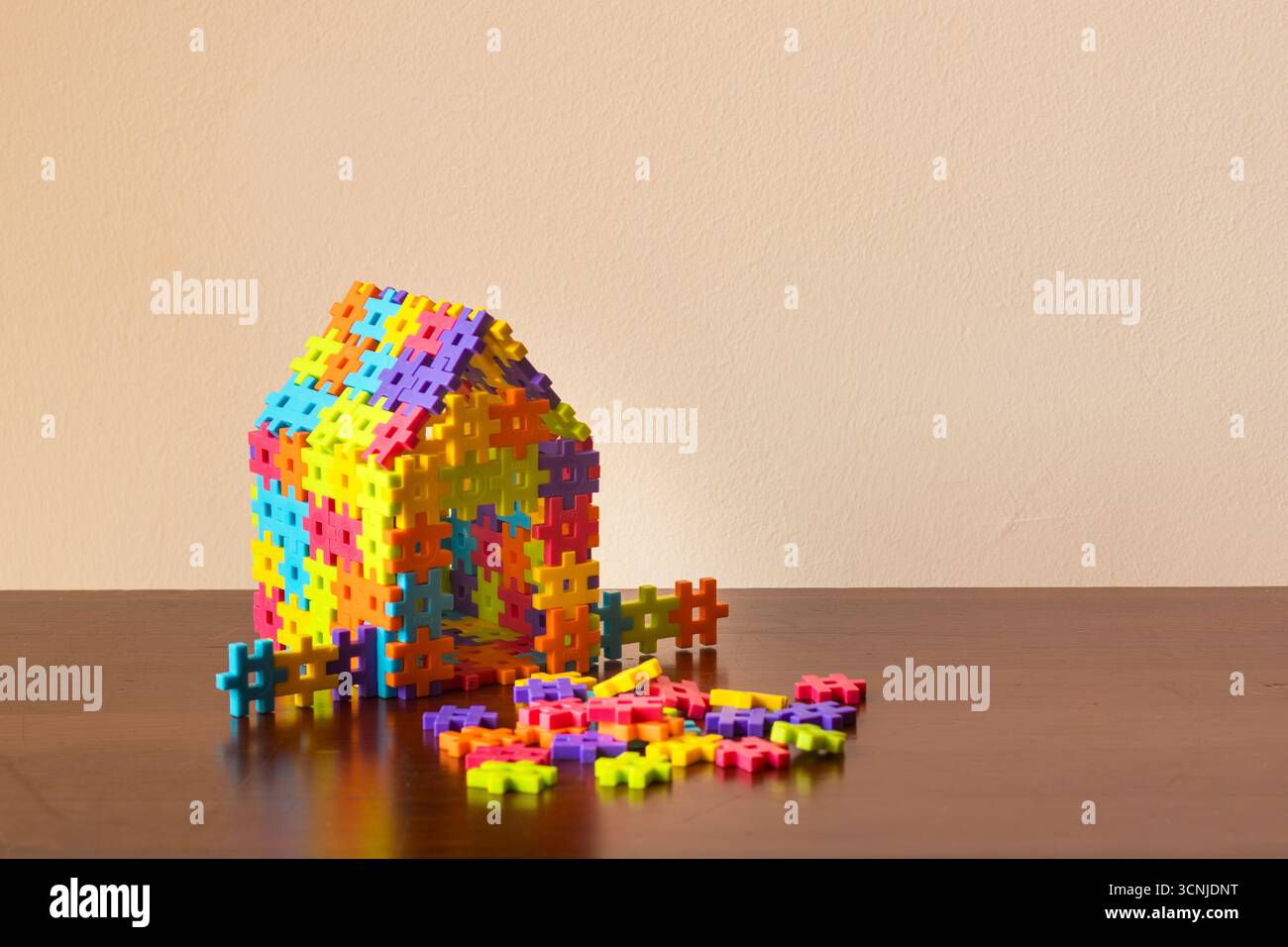Bunte, ineinander greifende Kunststoffziegel, die ein Haus auf einem Holztisch bilden, symbolisieren Konstruktion, Spiel und Immobilieninvestition Stockfoto