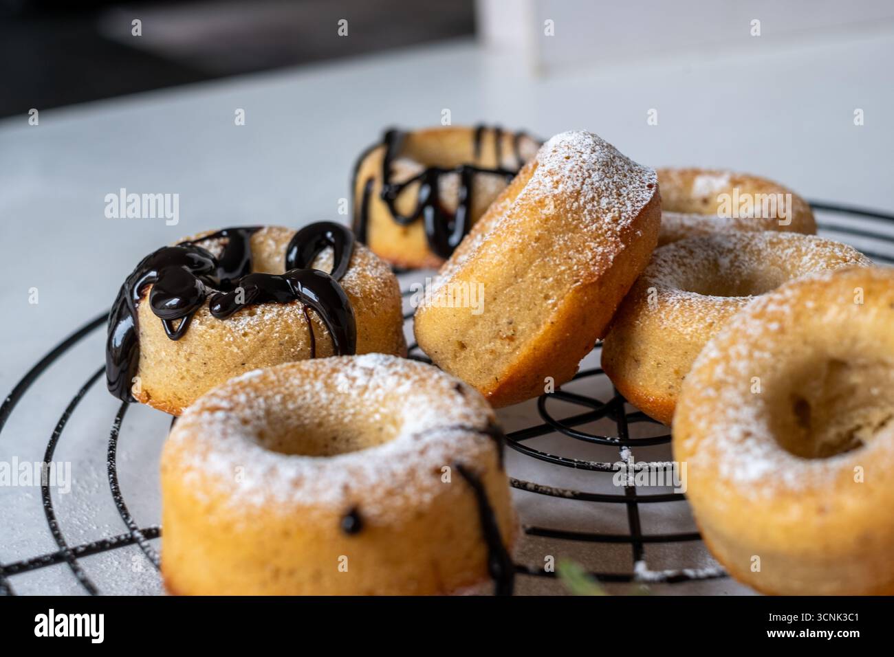Köstliche Donuts kühlen auf einem Gitter mit Puderzucker und Schokoladennebel ab und schaffen eine warme und einladende Atmosphäre für Dessertliebhaber Stockfoto